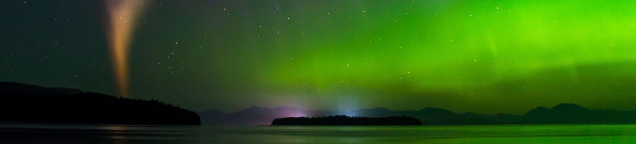 Naona Peaches Wallin - Aurora borealis above the ocean with violet, orange and green hues in the sky